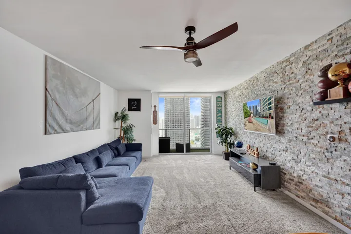 Textured stone accent wall, ceiling fan, carpeted flooring, and balcony access with sliding glass doors