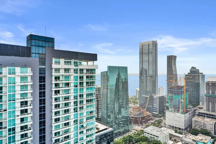 High-rise building with multiple balconies, a rooftop structure, and a city skyline backdrop featuring water