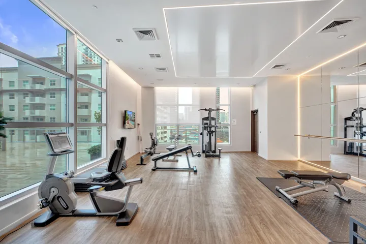 Spacious fitness area featuring wood-finish flooring, full-height windows, a mirrored wall with integrated lighting, and recessed ceiling lighting