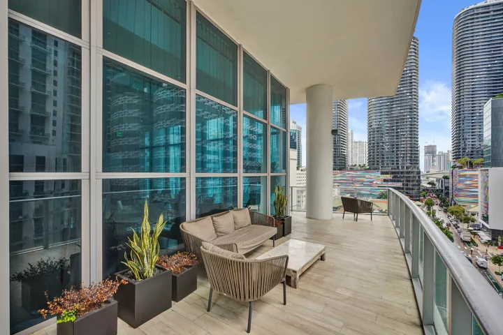 Expansive balcony featuring wood-finish flooring, a contemporary glass and metal railing, floor-to-ceiling windows, and a large support column