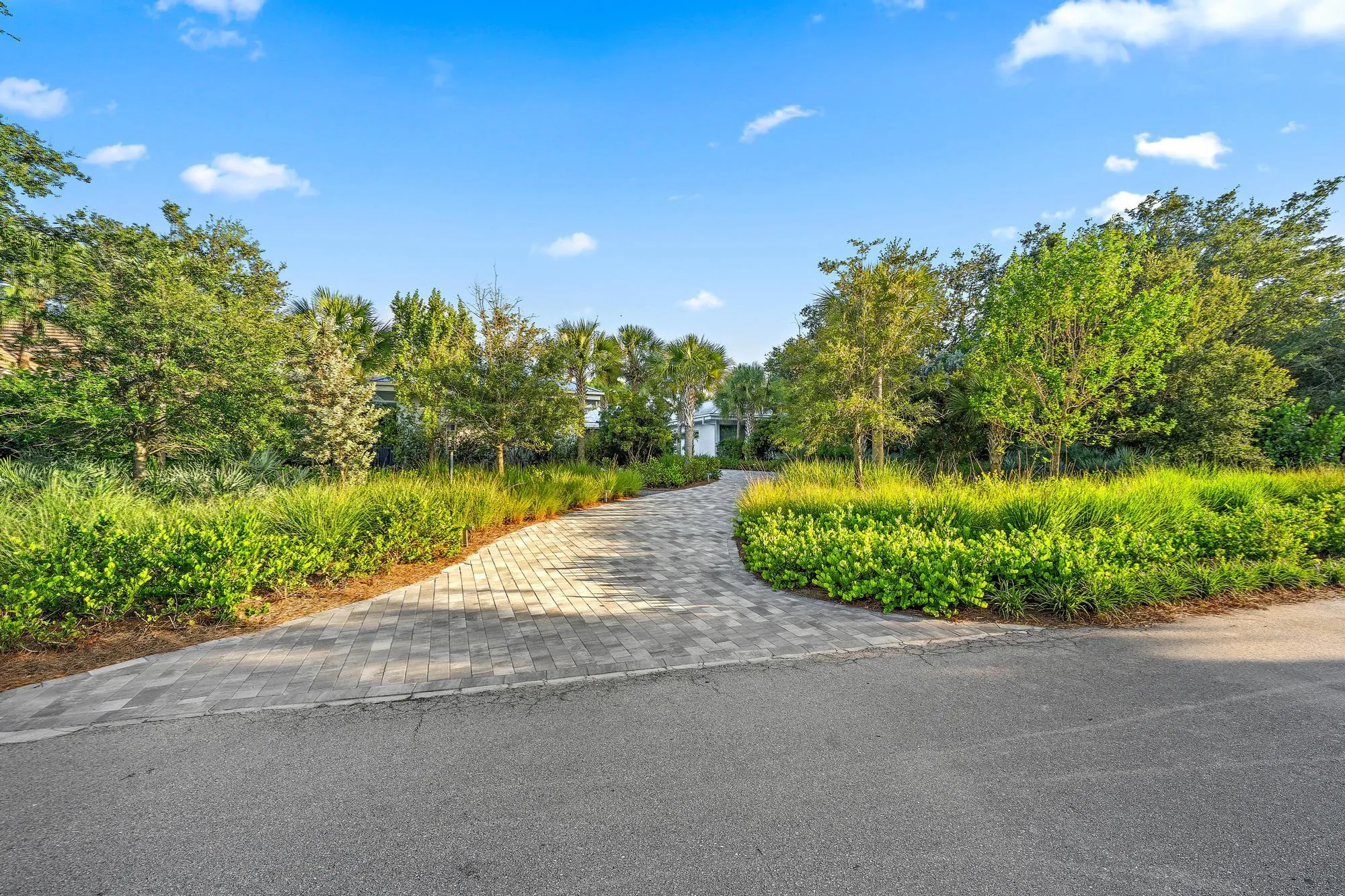 Paver driveway featuring a landscaped border of mature trees and shrubbery
