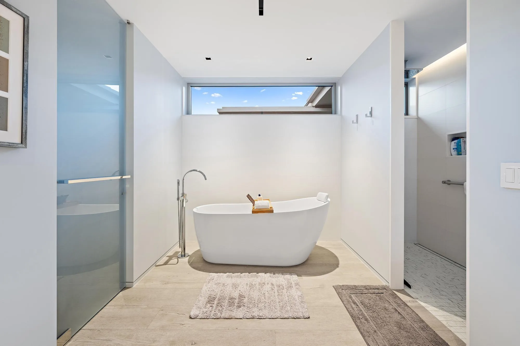 Freestanding soaking tub with floor-mounted faucet, frosted glass shower enclosure, and transom window