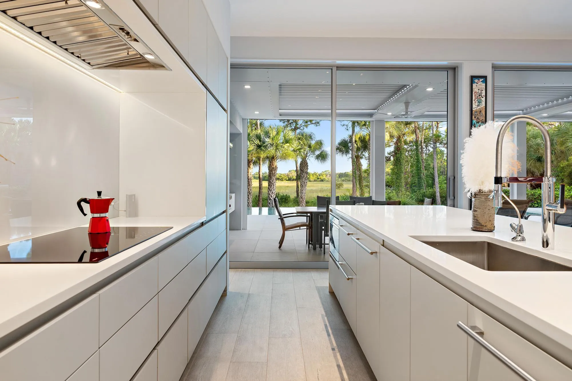 Modern kitchen featuring white cabinetry with handleless design, quartz countertops, stainless steel undermount sink with contemporary faucet, and integrated appliances
