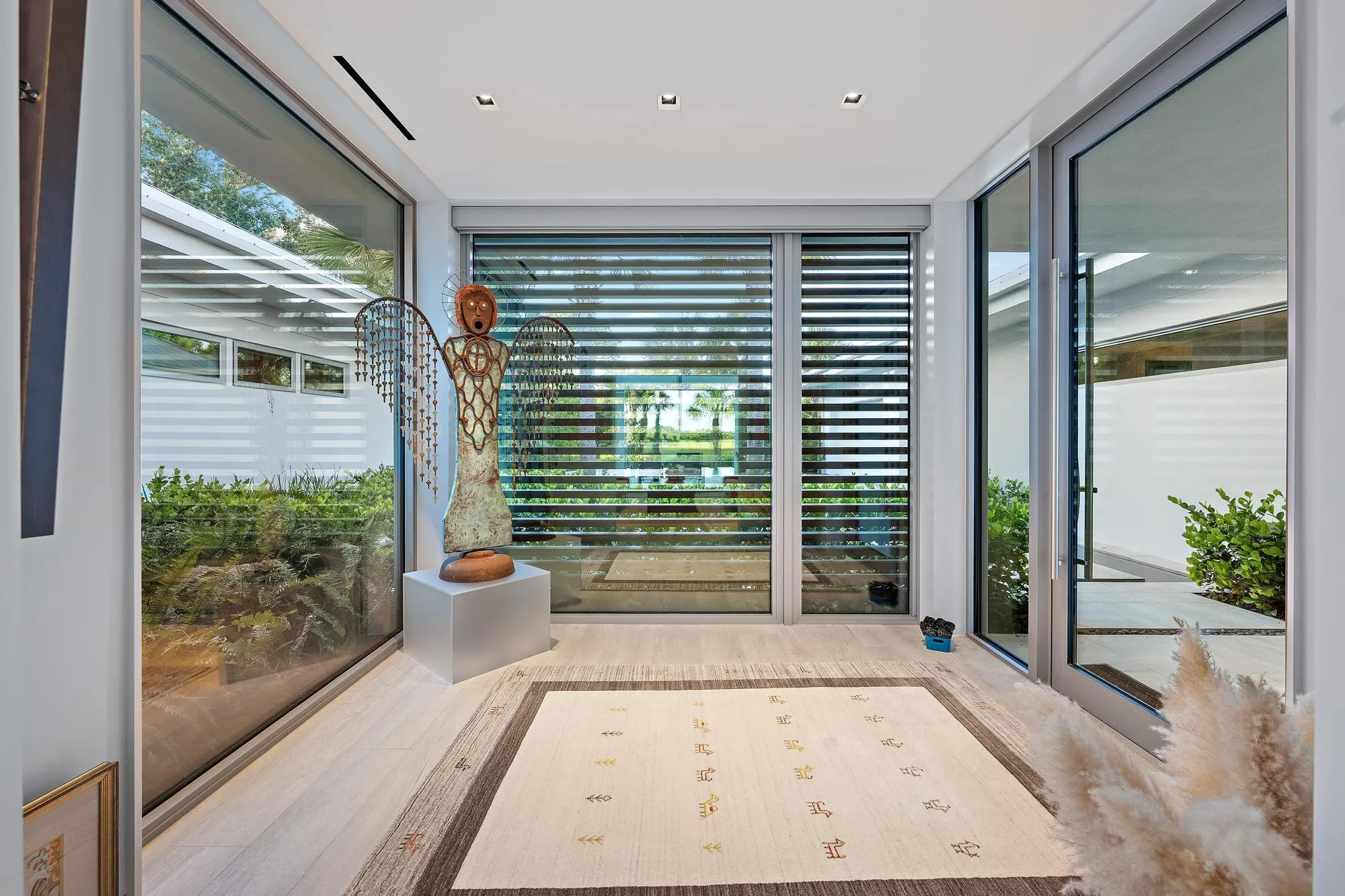 Light-filled sunroom with floor-to-ceiling glass panels, horizontal louvre shutters, and light wood-finish flooring