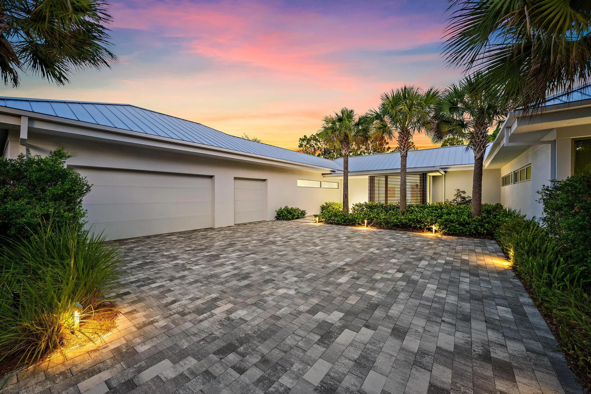 Modern exterior featuring a metal roof, two-car garage, and a paver driveway