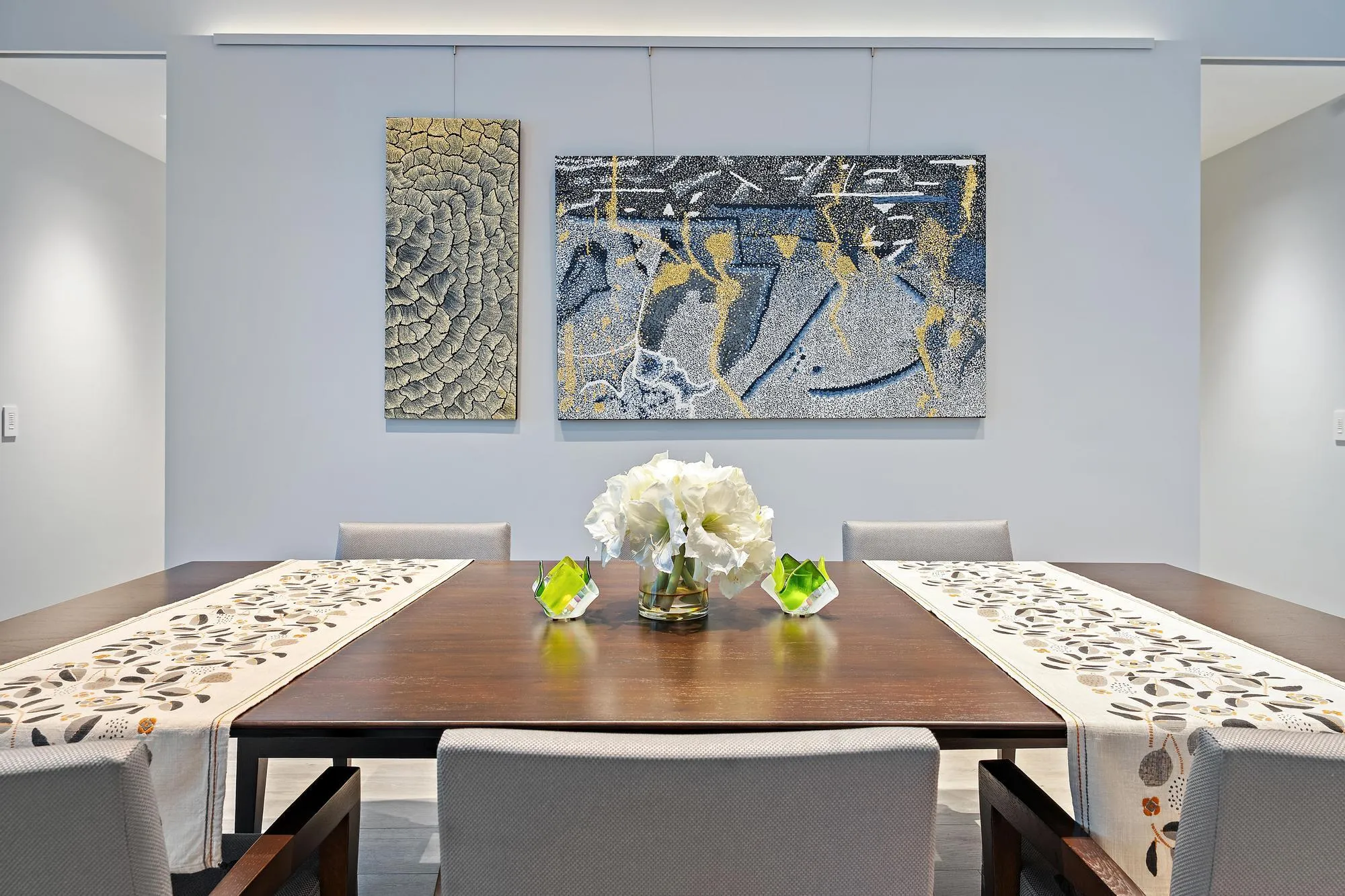 Wood-finish dining table with upholstered chairs, recessed lighting, and wall-mounted art display system