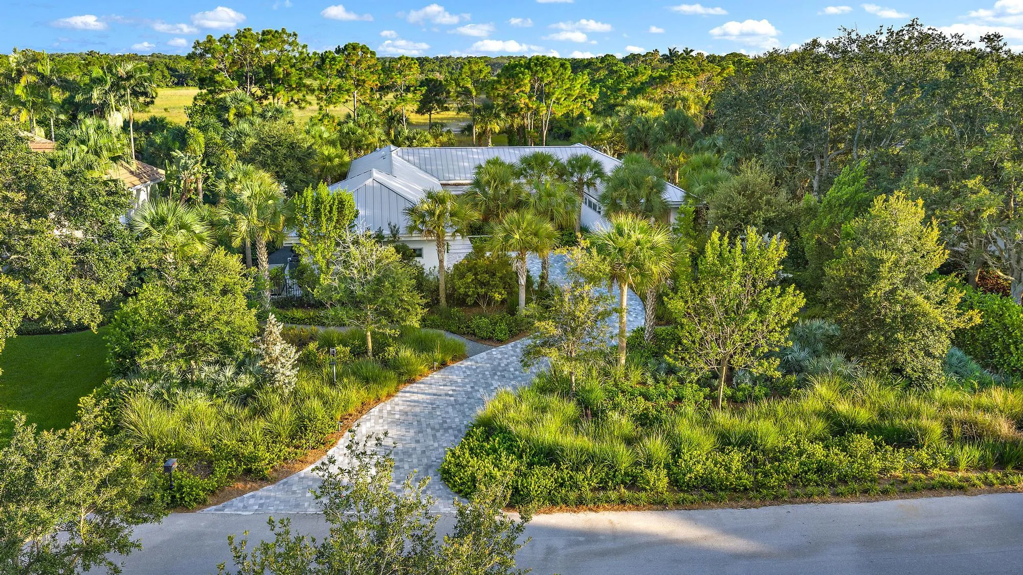 Modern architectural design with a metal roof, surrounded by lush landscaping and a paved driveway