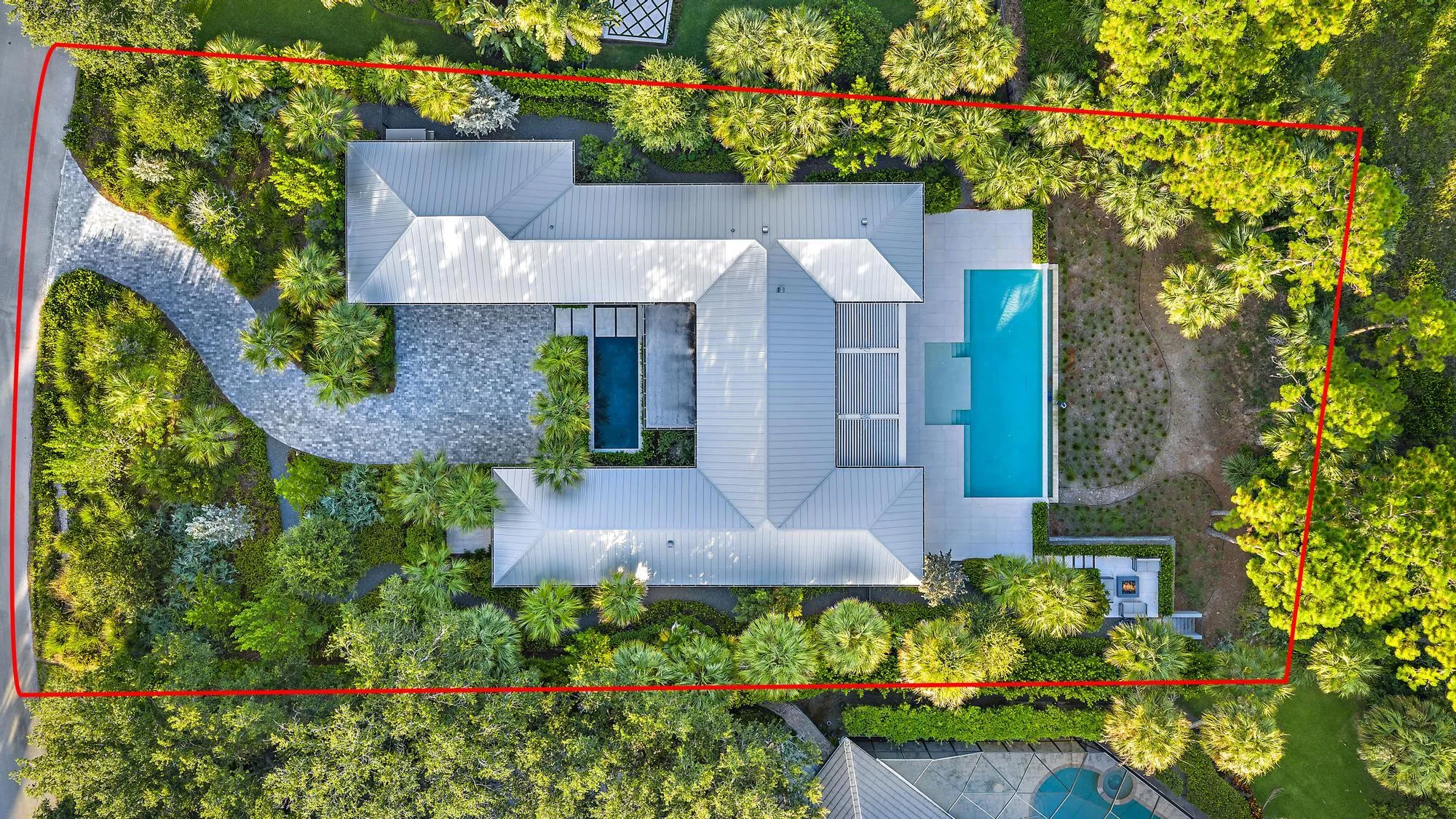 Expansive property featuring a winding paver driveway, lush landscaping, two distinct swimming pools, and a private outdoor lounge area