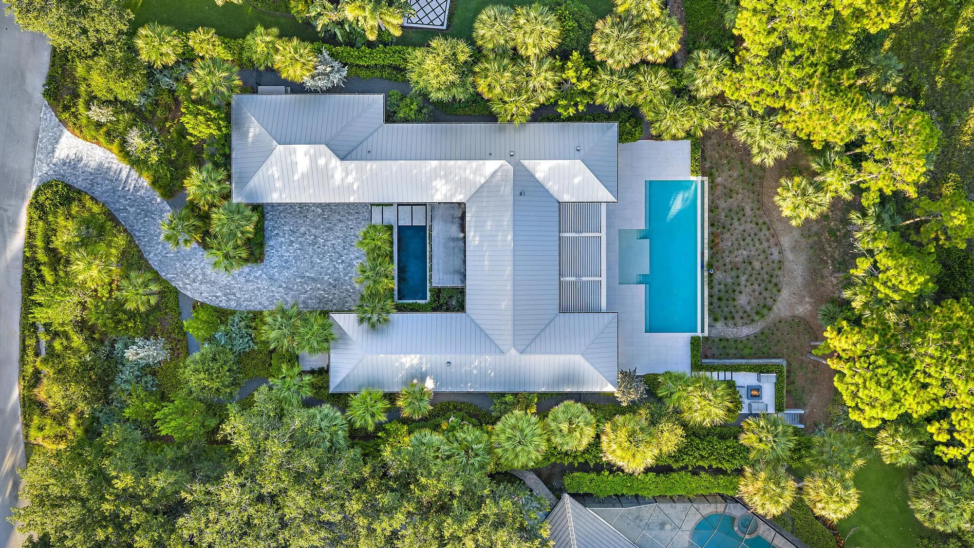 Modern architecture with a metal roof, two exterior pools, extensive landscaping, and a curvilinear paver driveway