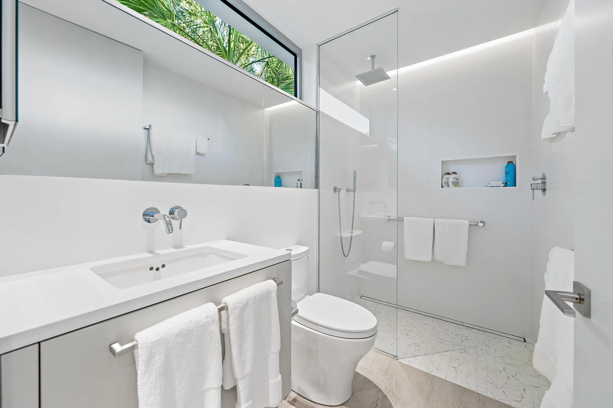 Modern bathroom featuring a vanity with an integrated sink, polished chrome wall-mounted faucet, a flush-mounted toilet, and a glass-enclosed shower with a rainfall showerhead