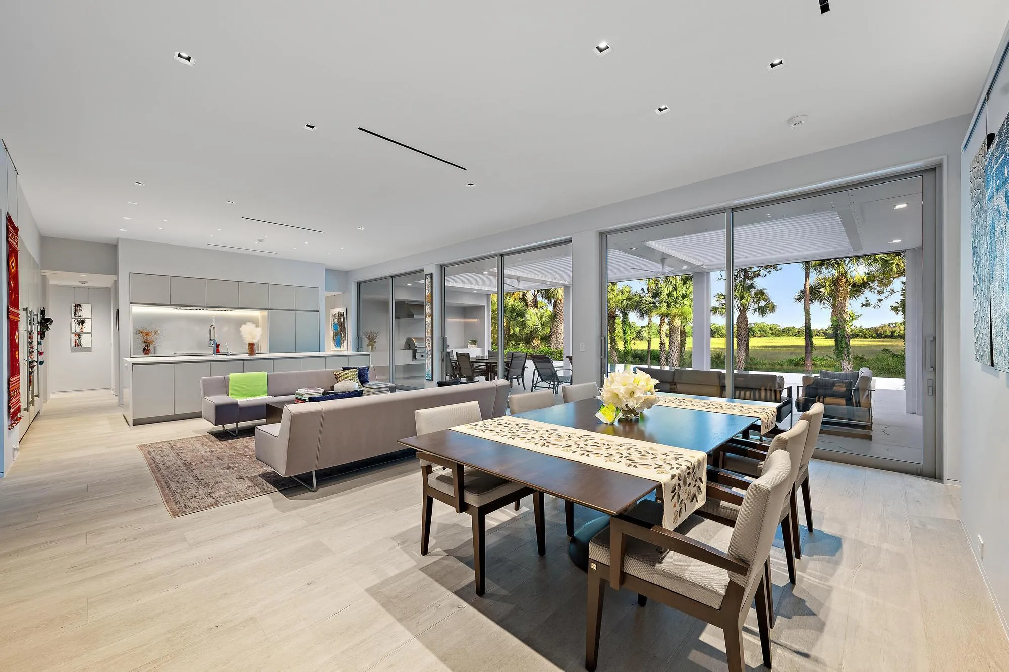 Open-concept living area featuring light wood-finish flooring, a contemporary kitchen with light cabinetry, and expansive sliding glass doors