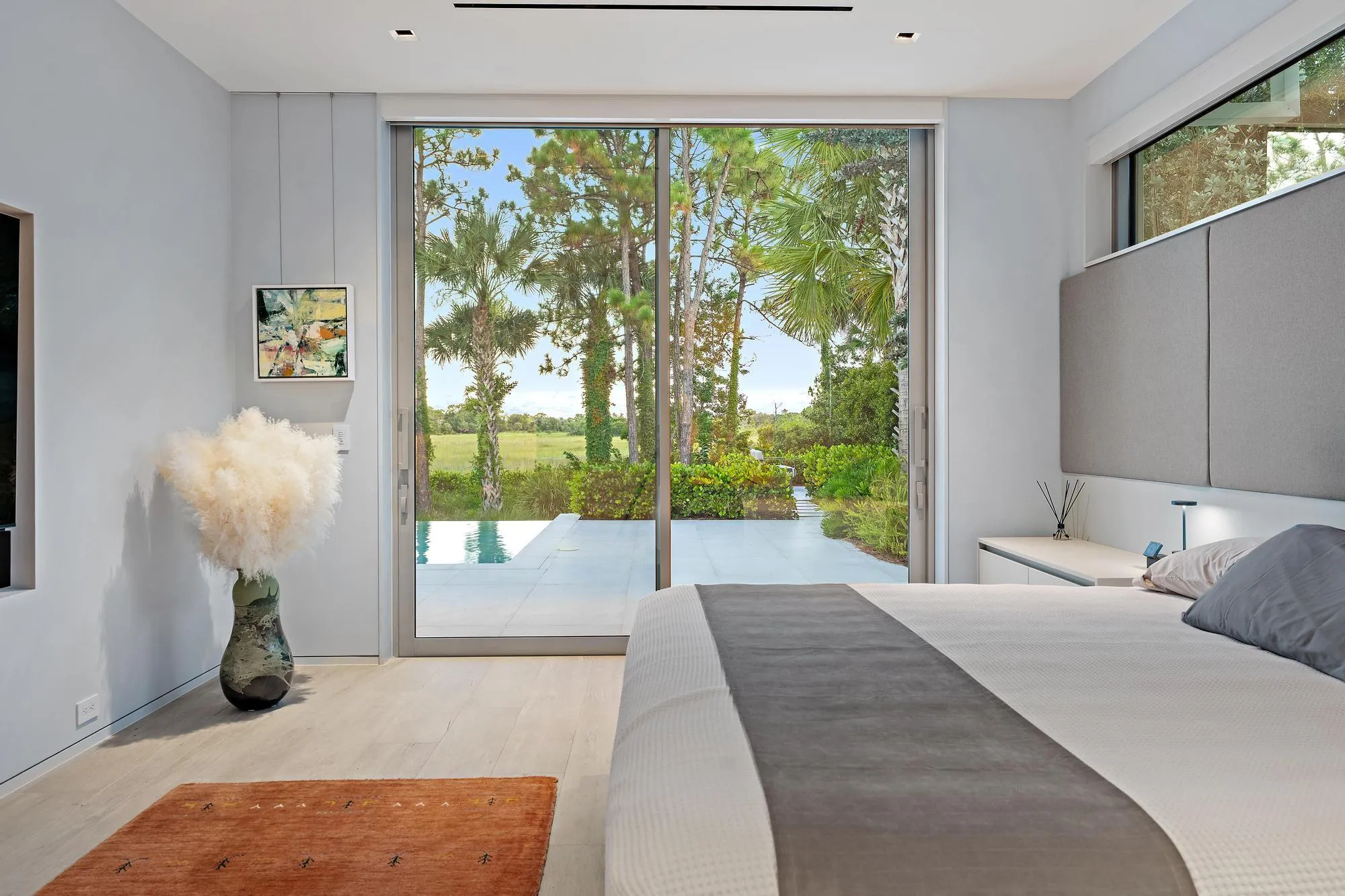 Expansive sliding glass doors, light wood-finish flooring, recessed ceiling lighting, and a built-in upholstered headboard
