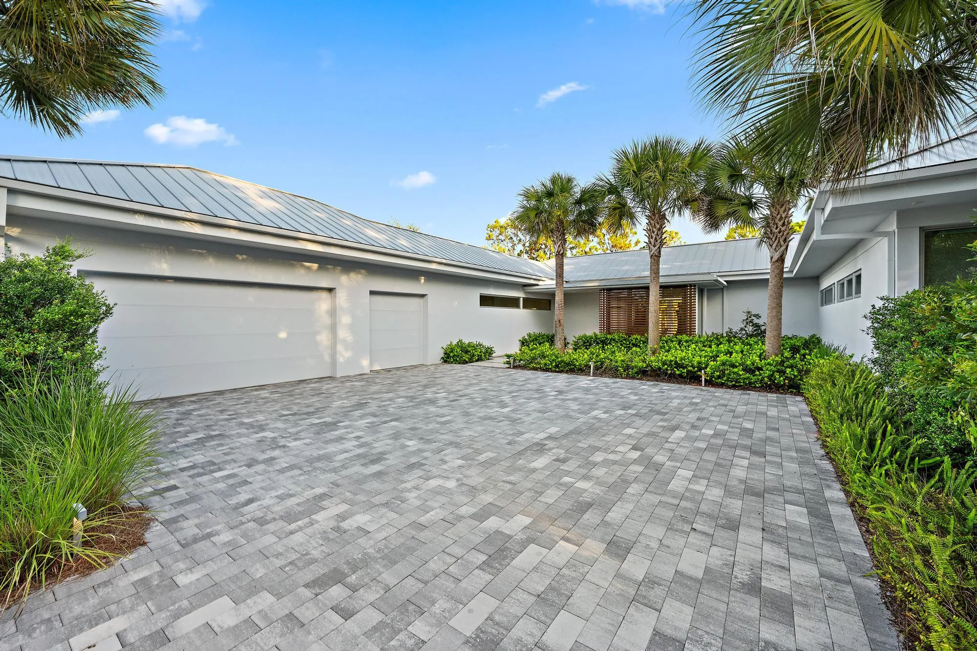 Paver driveway, mature palm trees, contemporary exterior, metal roof, and integrated landscaping
