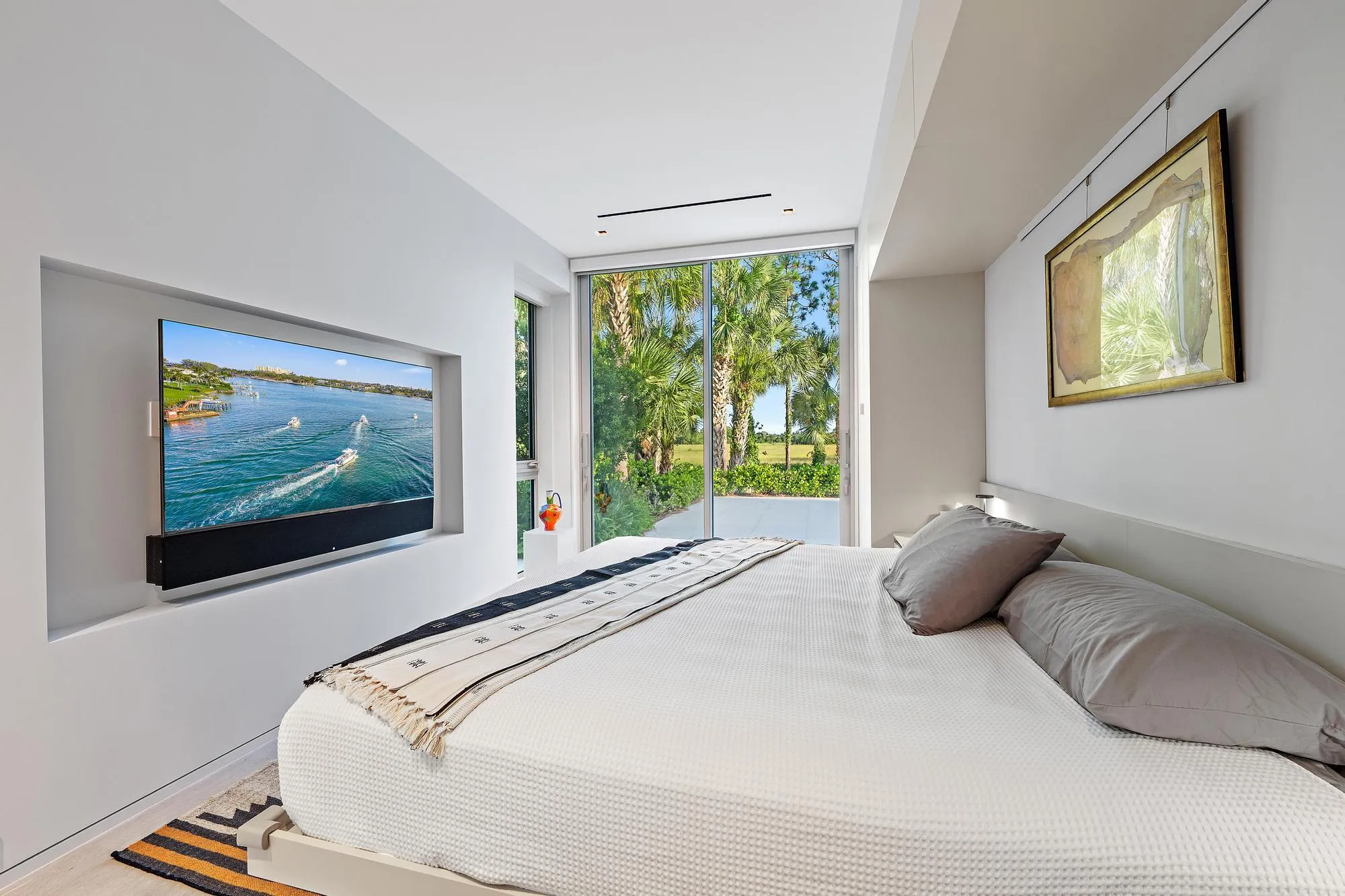 Recessed wall-mounted television with soundbar, full-height sliding glass doors, and a built-in headboard with integrated lighting
