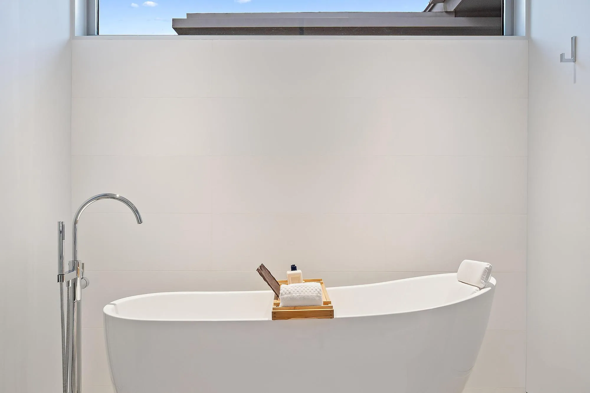 Modern spa-inspired soaking tub with curved silhouette and seamless white finish, paired with a contemporary floor-mounted freestanding tub filler featuring an arched spout