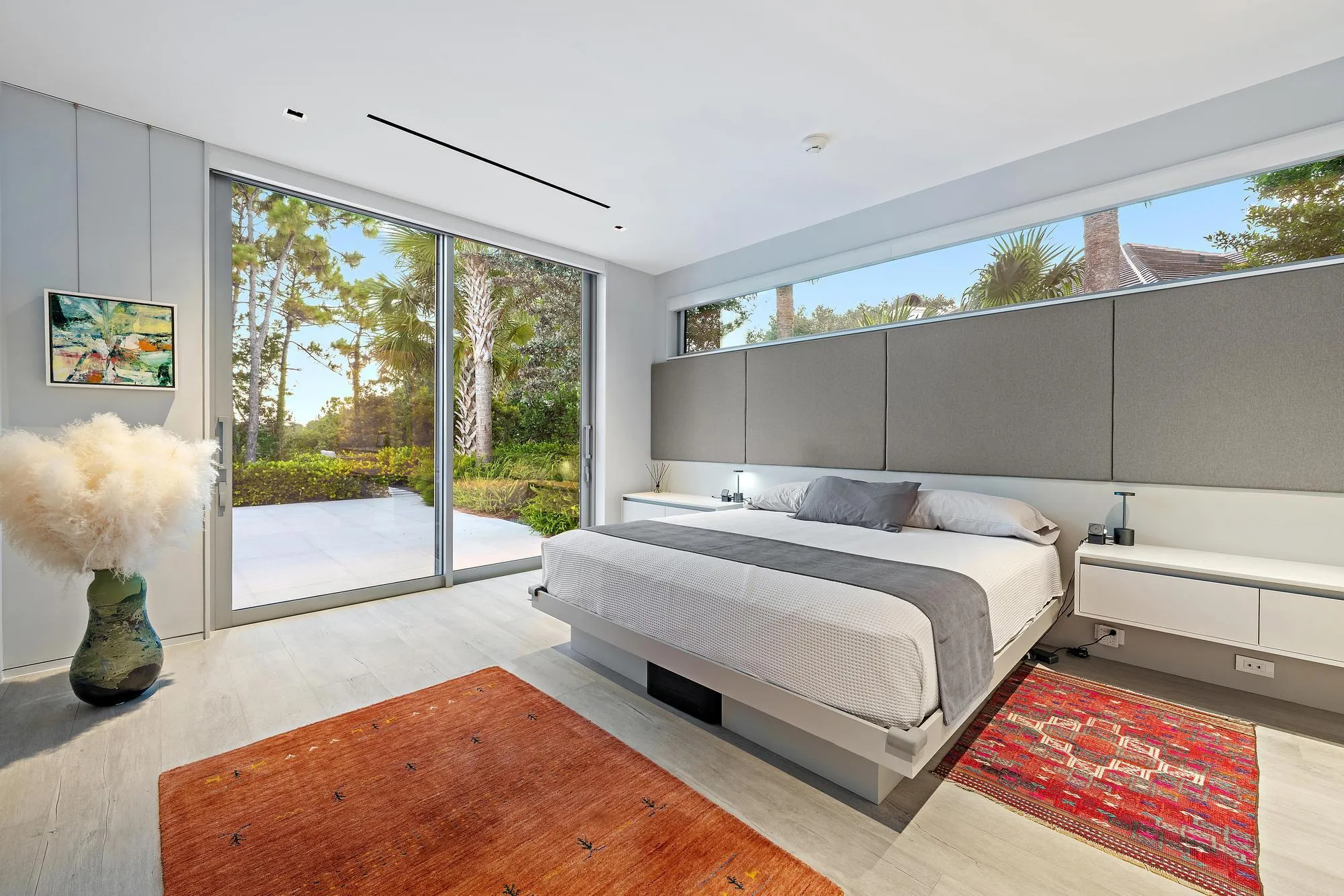 Sliding glass doors opening to an outdoor patio, wood-finish flooring, integrated linear ceiling lighting, and transom windows
