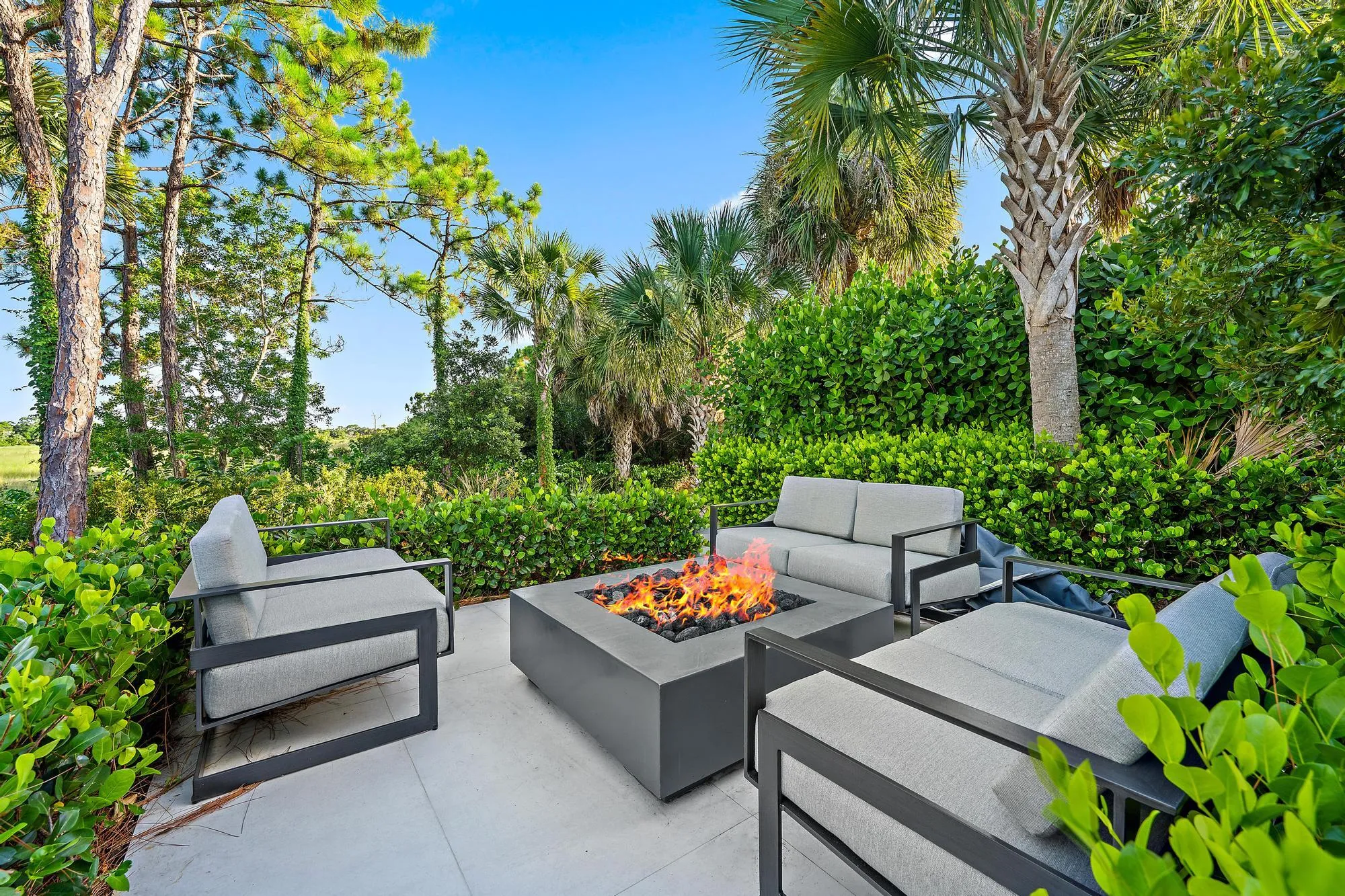 Paved patio with a built-in fire pit, surrounded by lush landscaping and mature trees