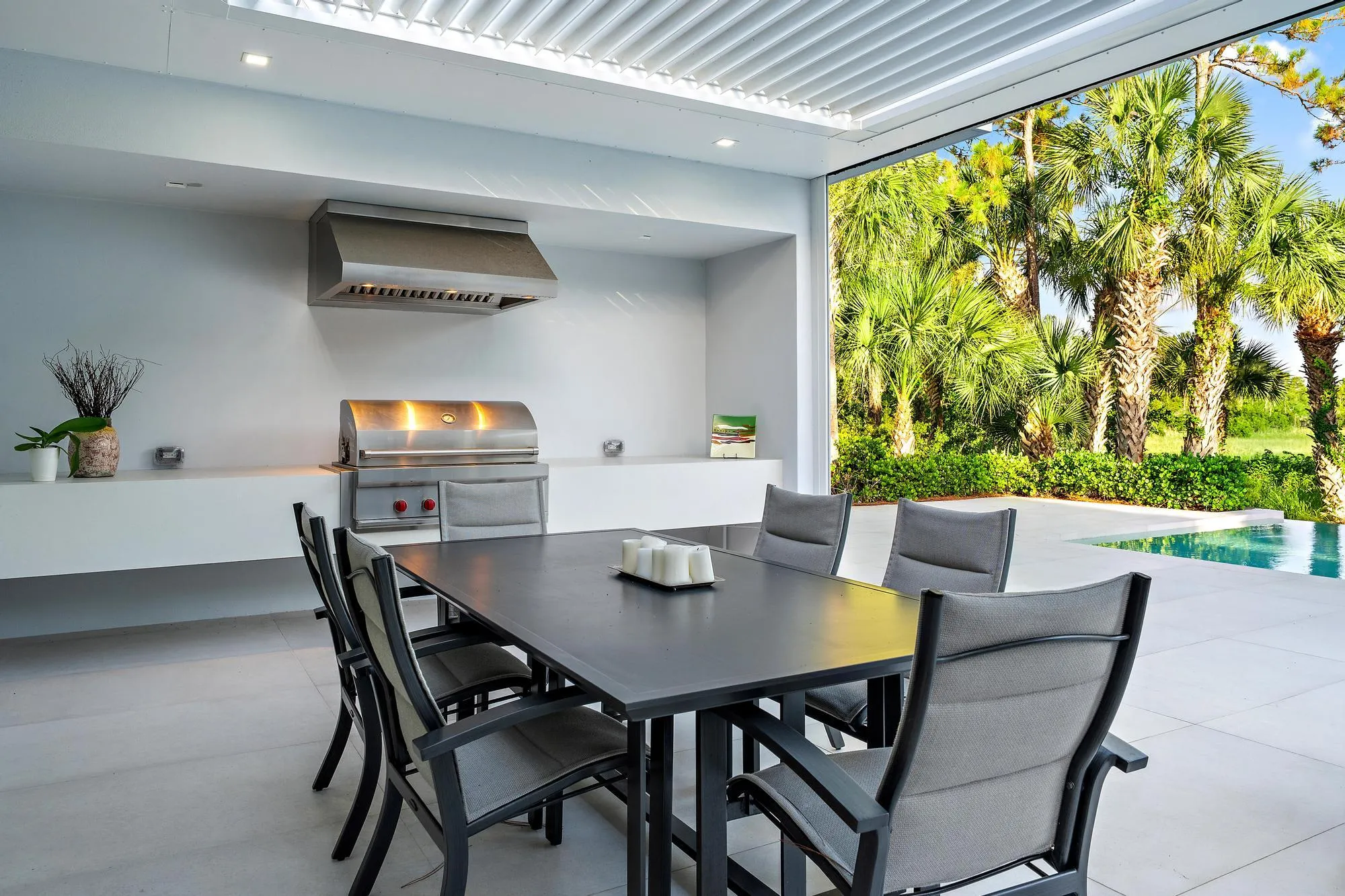 Outdoor kitchen with stainless steel grill and range hood, integrated countertop, built-in recessed lighting, and a swimming pool