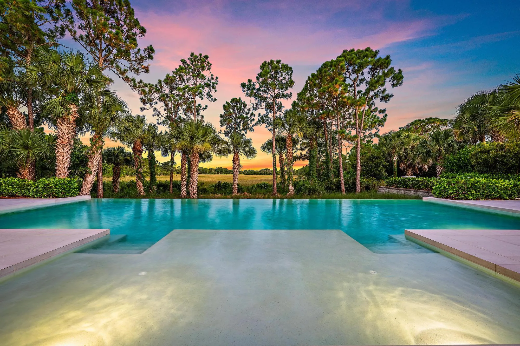 Infinity-edge pool with integrated steps, surrounded by lush tropical landscaping and mature trees