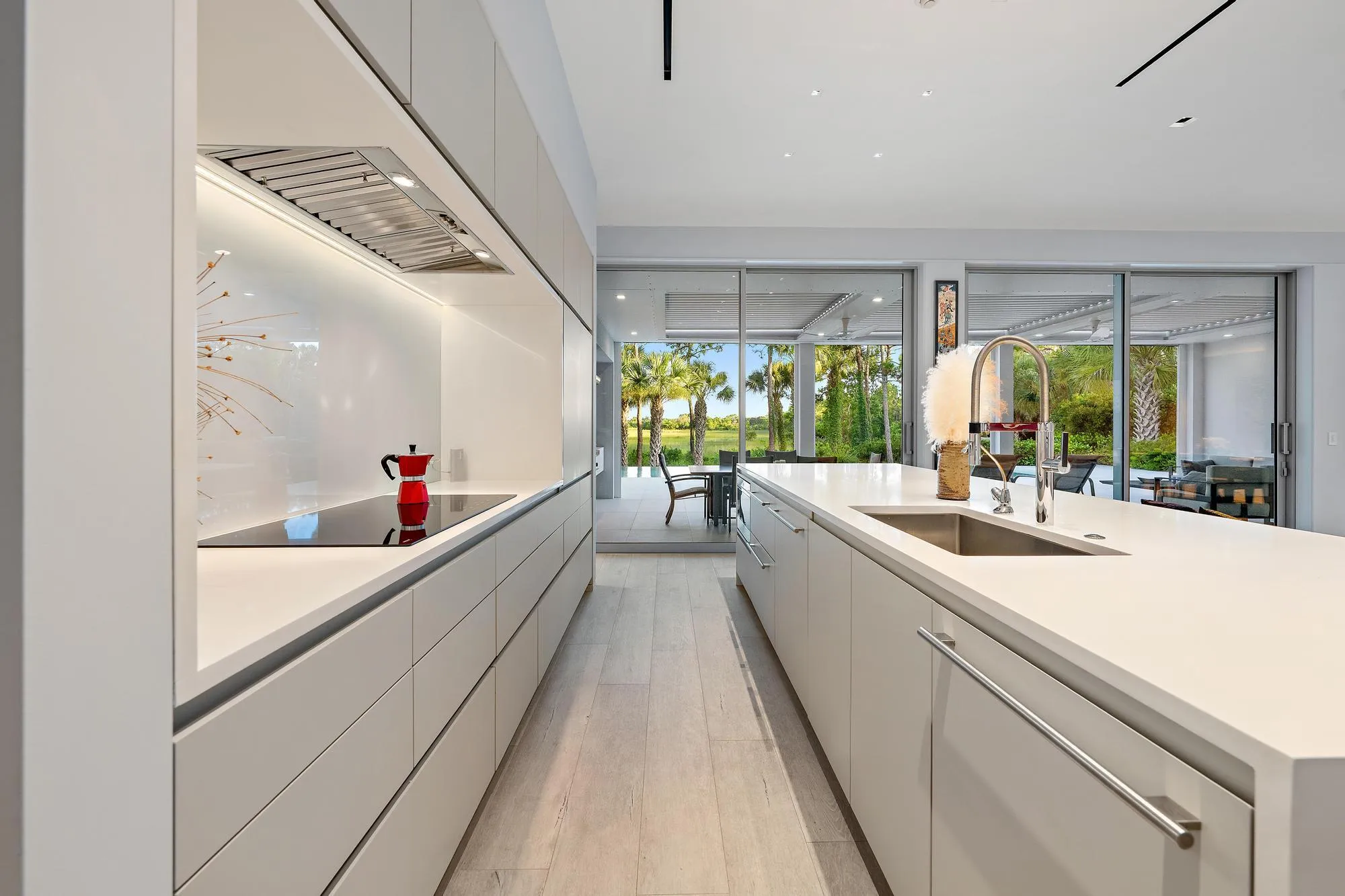 Modern kitchen featuring white flat-panel cabinetry, light wood-finish flooring, a stainless steel sink, and a cooktop with an integrated range hood
