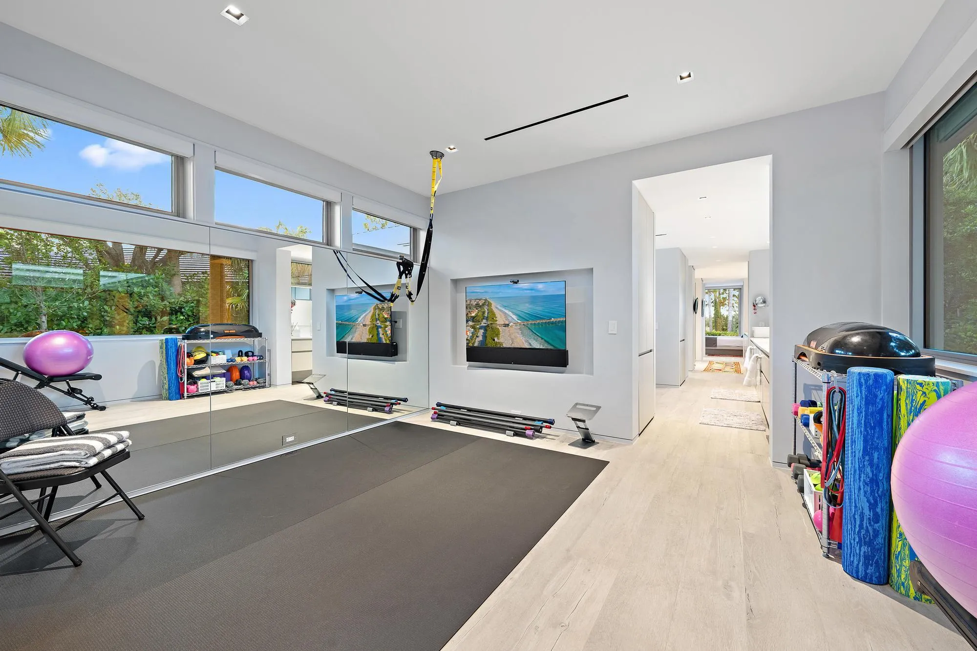 Expansive fitness space featuring light wood-finish flooring, full-height wall mirrors, and large windows with transom panels