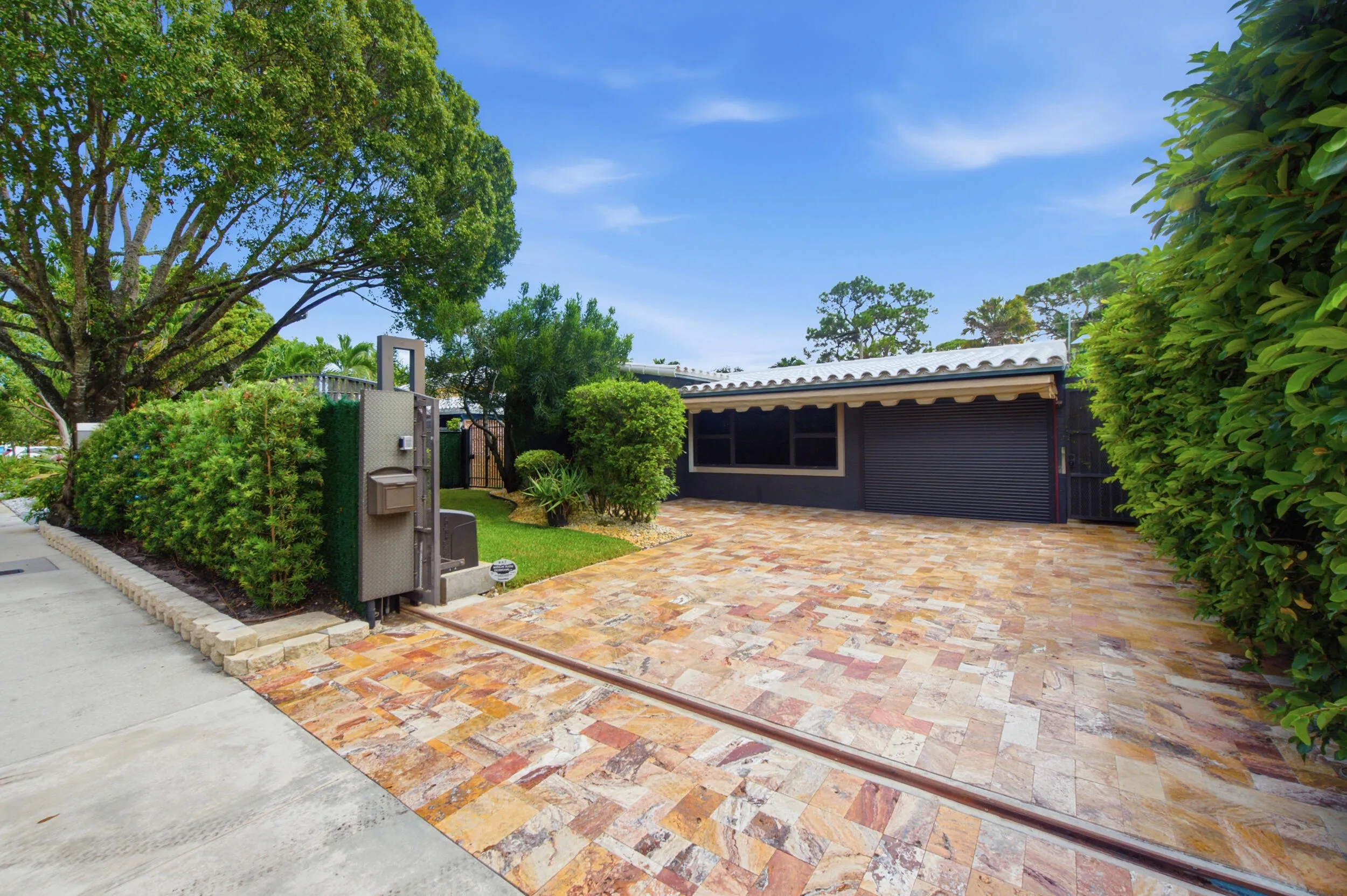 Exterior featuring a paver driveway, mature landscaping, and a secure entry gate
