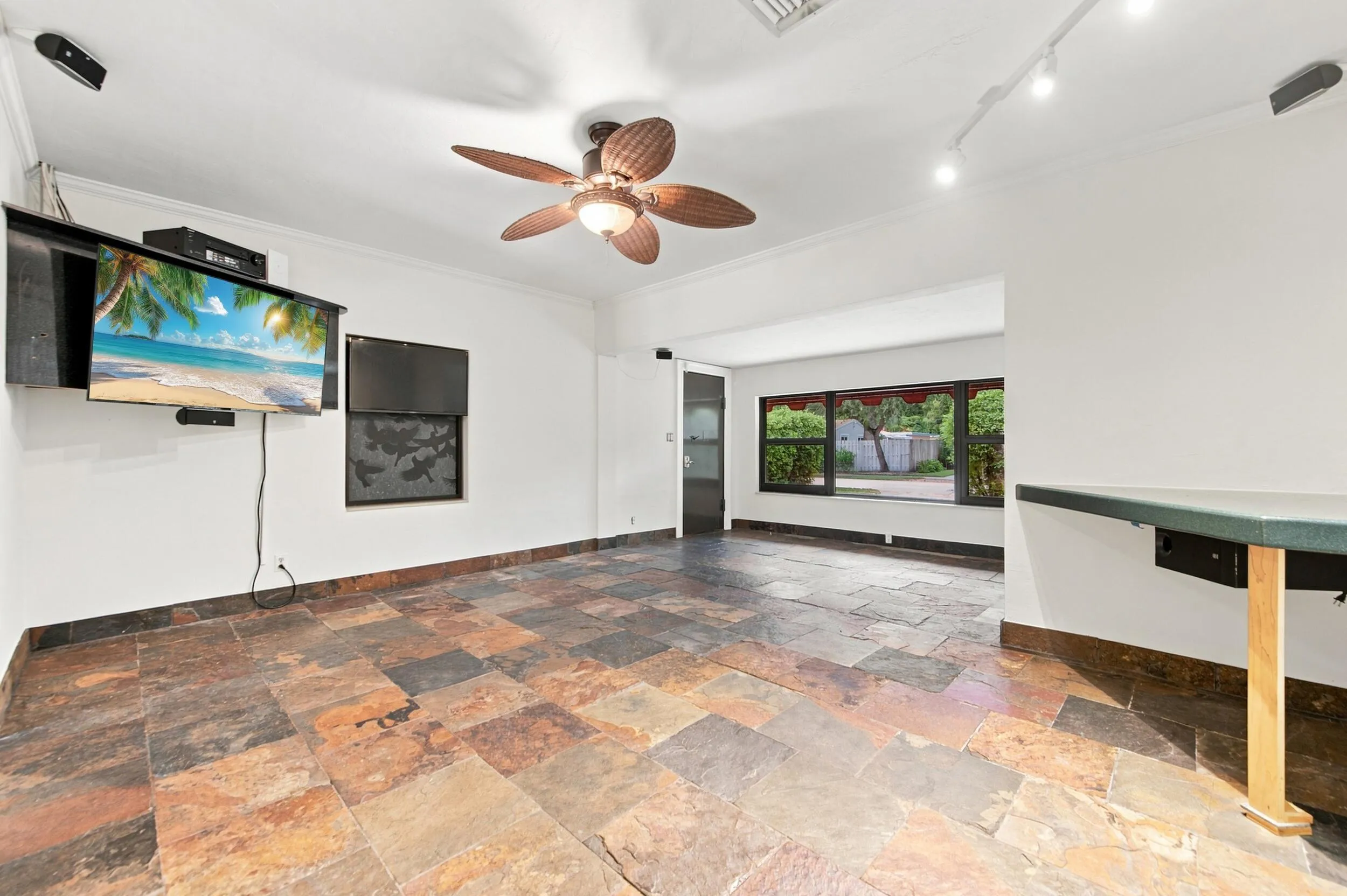 Spacious room featuring multi-toned stone tile flooring, a ceiling fan with integrated lighting, track lighting, and large windows