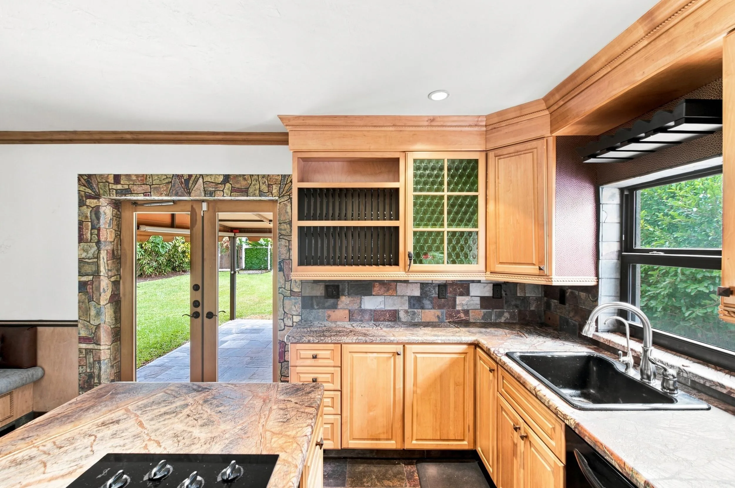 Kitchen featuring wood cabinetry, stone countertops, integrated cooktop, undermount sink, and stone backsplash
