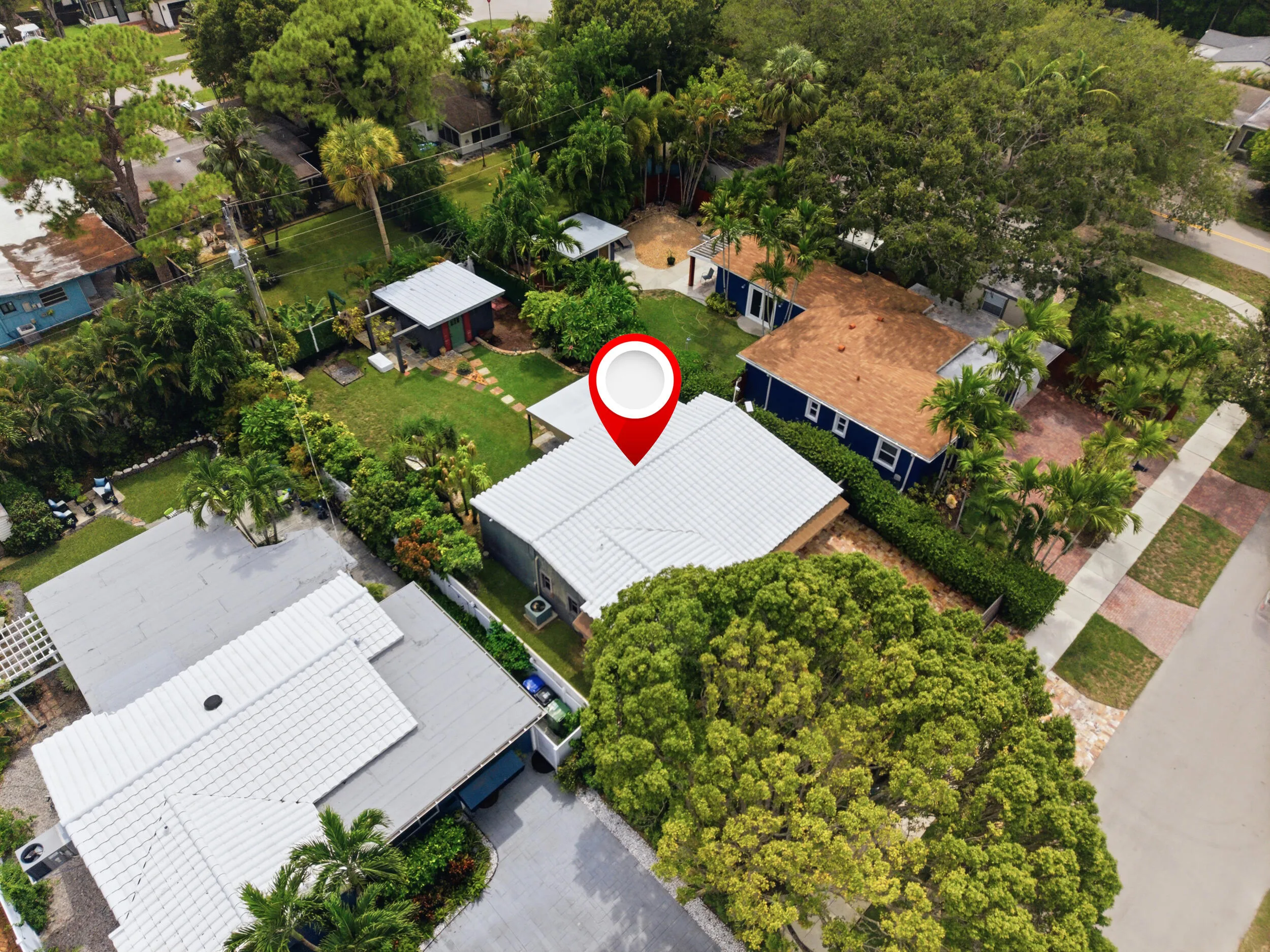Property featuring a white tile roof, mature landscaping, and a surrounding residential area