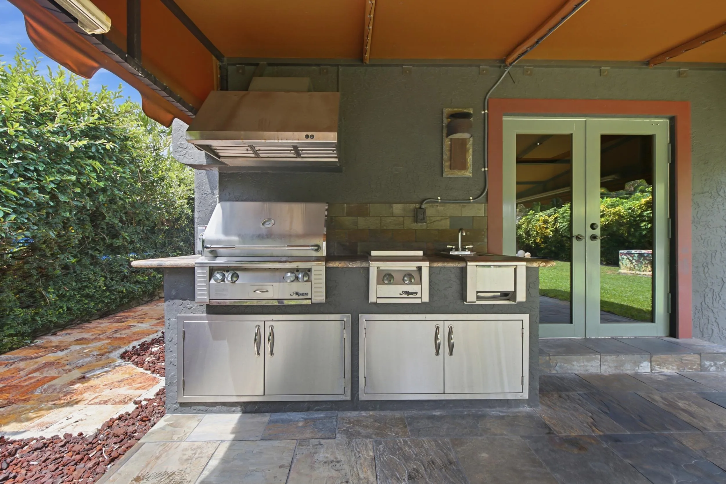 Outdoor kitchen featuring a built-in stainless steel grill, range hood, and sink