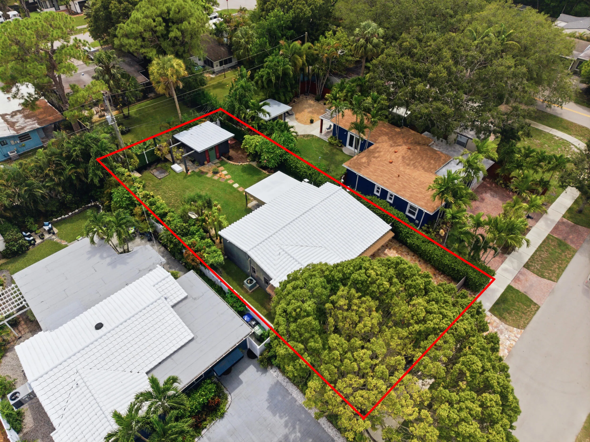 Property featuring a main residence with a white metal roof, a detached accessory structure with a metal roof, and an expansive lawn with mature trees