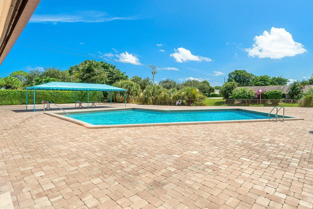 Community swimming pool with a spacious brick-paver deck and shaded seating area.