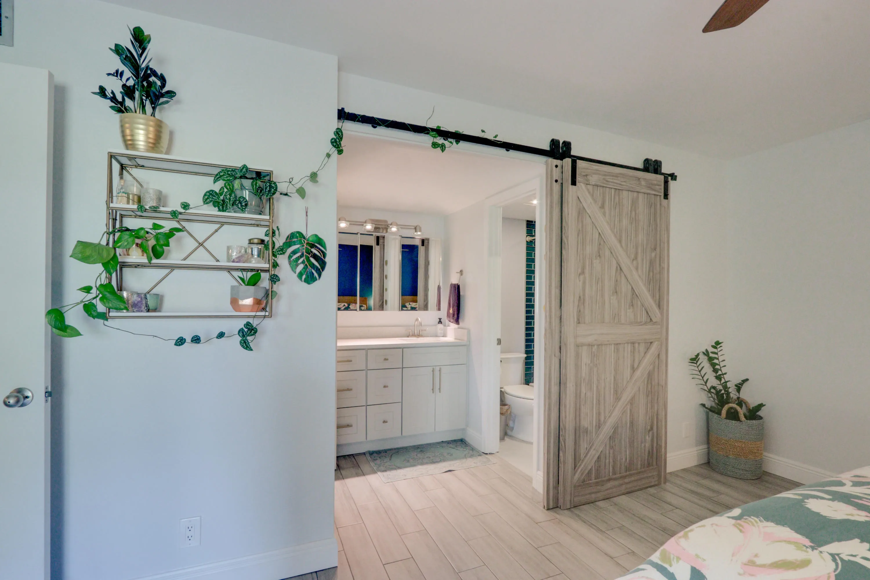Wood-finish flooring, barn door entry, dual vanity, contemporary shelving unit, and ceiling fan