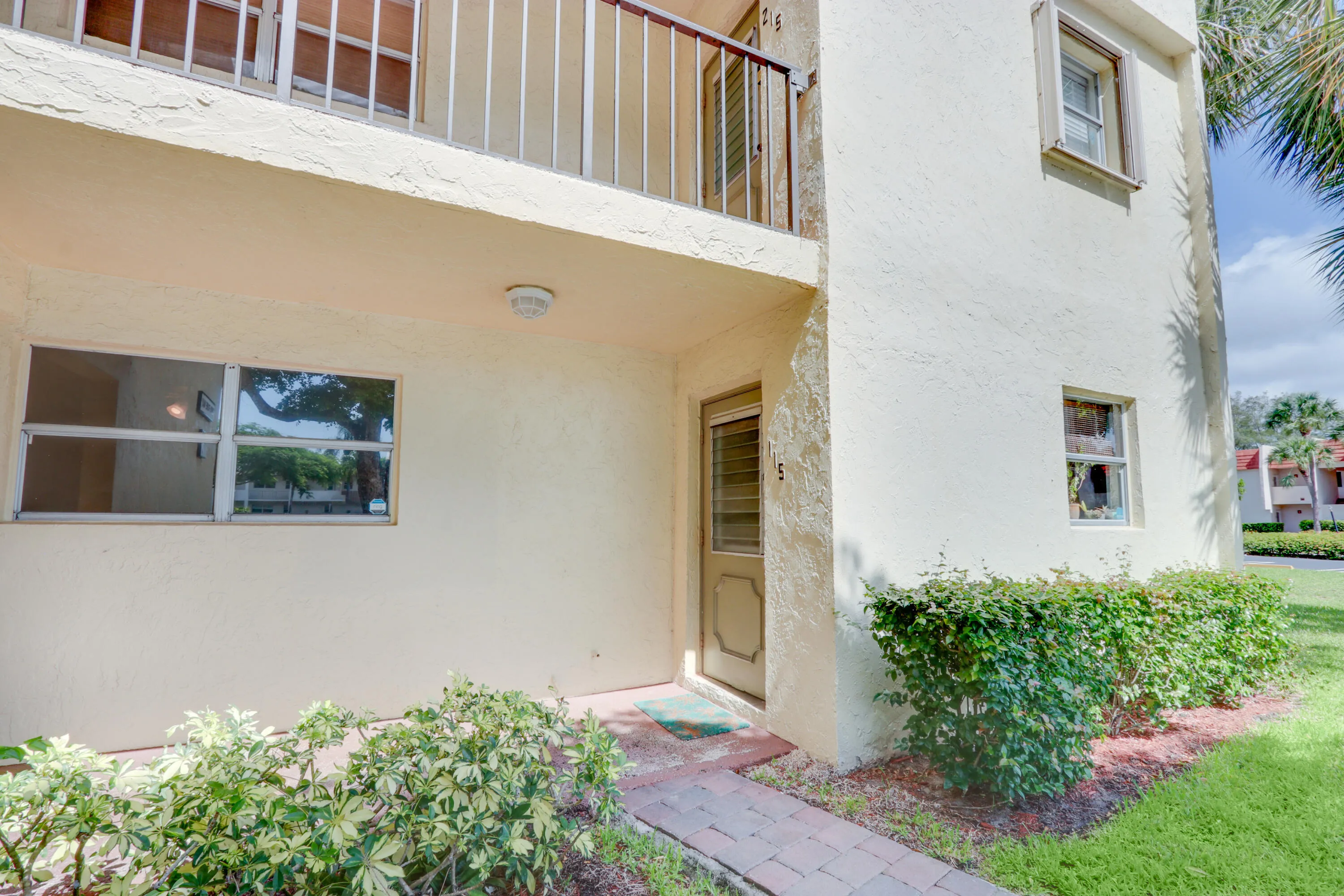 Stucco exterior with a balcony, brick paver walkway, and established landscaping