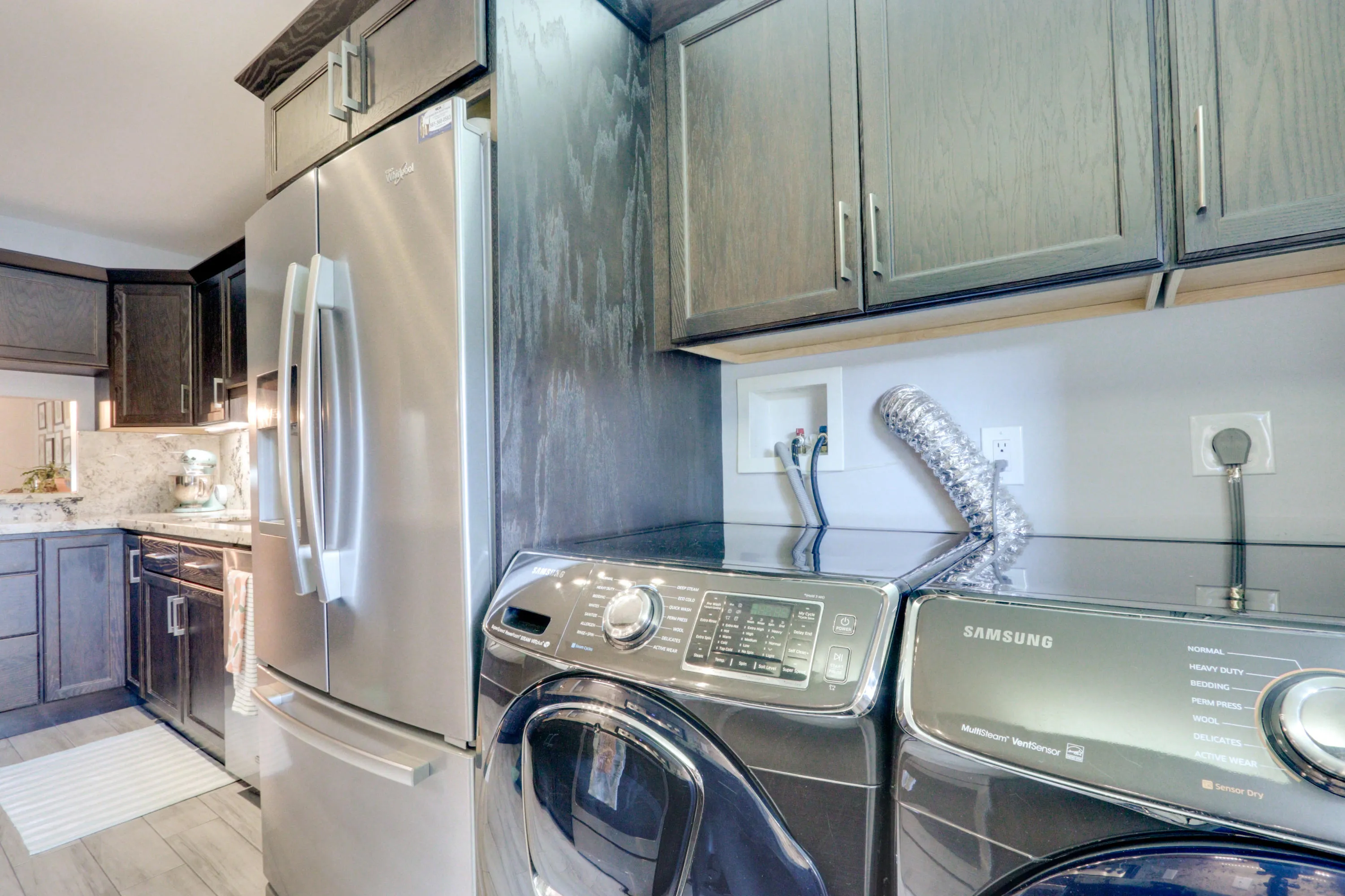 Dark wood-finish cabinetry with silver hardware, stainless steel refrigerator, and light-toned countertop