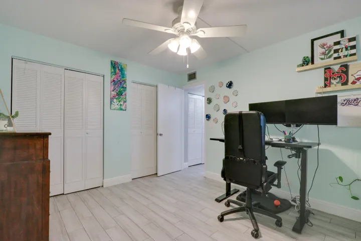 Light-toned wood-finish flooring, two sets of bi-fold louvered doors, and a ceiling fan with integrated lighting