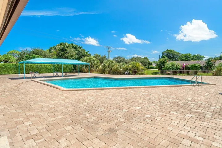 Community swimming pool with a spacious brick-paver deck and shaded seating area.