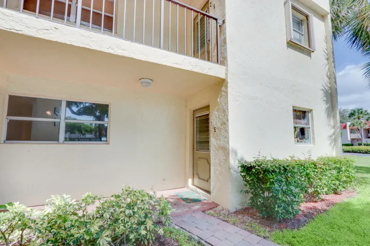 Stucco exterior with a balcony, brick paver walkway, and established landscaping