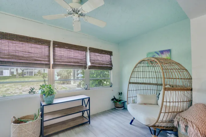 Enclosed patio featuring light wood-finish flooring, multiple windows with woven blinds, and a ceiling fan