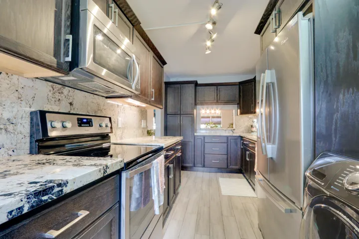 Kitchen featuring dark wood-finish cabinetry, stainless steel appliances, speckled stone countertops, and wood-finish flooring