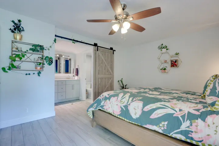 Wood-finish flooring throughout, ceiling fan with integrated lighting, and a barn door entry to the bathroom