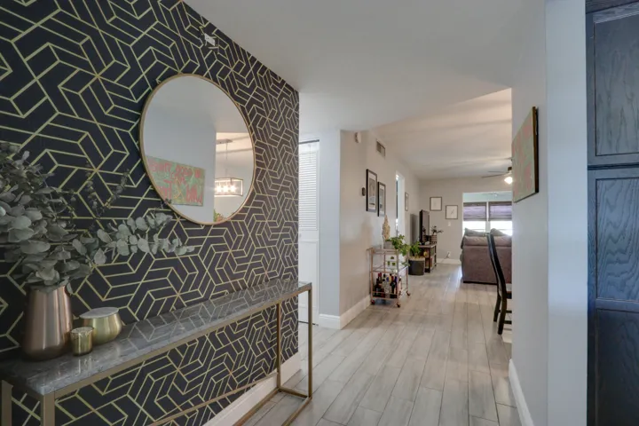 Patterned accent wall, wood-finish flooring, recessed lighting, built-in cabinetry, and a round wall mirror