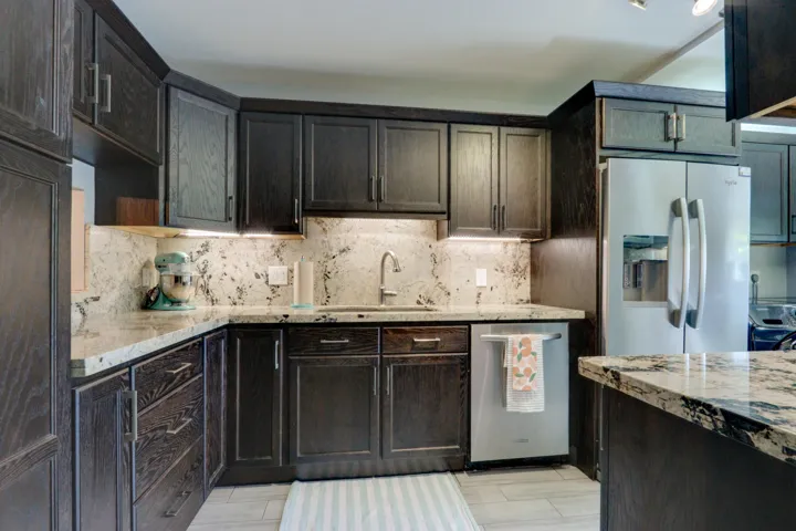 Dark wood-finish cabinetry with silver-tone hardware, light-toned countertops, integrated stainless steel appliances, and under-cabinet lighting