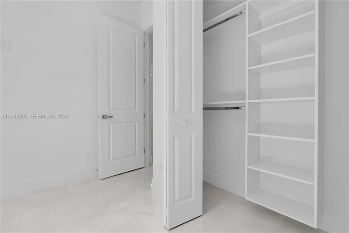 Custom walk-in closet featuring floor-to-ceiling built-in shelving and dual hanging rods, paired with polished tile flooring and a solid-core paneled door