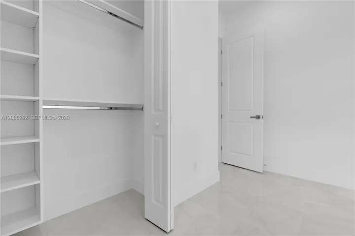 Walk-in closet featuring floor-to-ceiling built-in shelving, dual metal clothing rods, a panel door, and large-format tile flooring