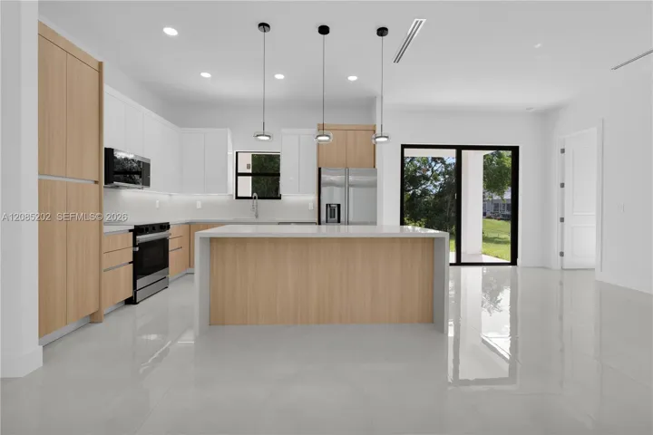 Kitchen featuring two-tone cabinetry with wood-finish and white flat-panel doors, a central island with a solid surface countertop, stainless steel appliances, and large-format porcelain tile flooring