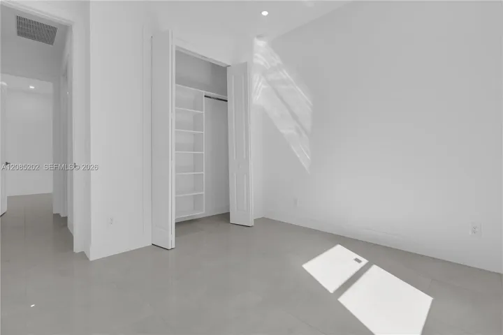 Neutral-toned tile flooring, recessed ceiling lighting, and a walk-in closet featuring built-in shelving and a hanging rod