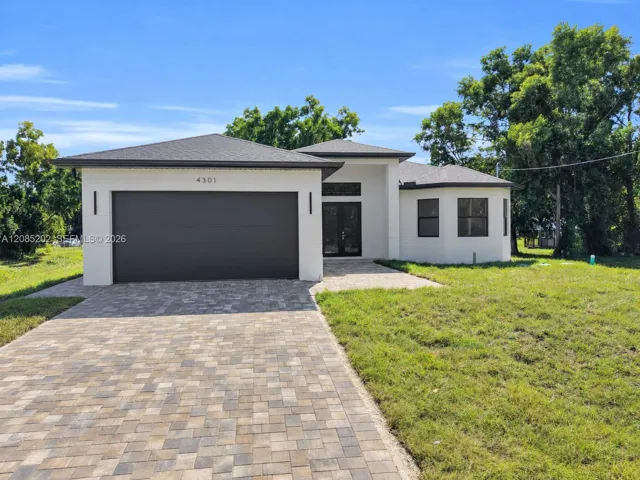Contemporary stucco exterior featuring a hip roof, multi-panel garage door, double-door entryway, and stone-paver driveway