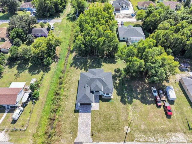Aerial perspective of a detached residence featuring a multi-gabled shingle roof, paved paver driveway, and a spacious lot with mature perimeter trees