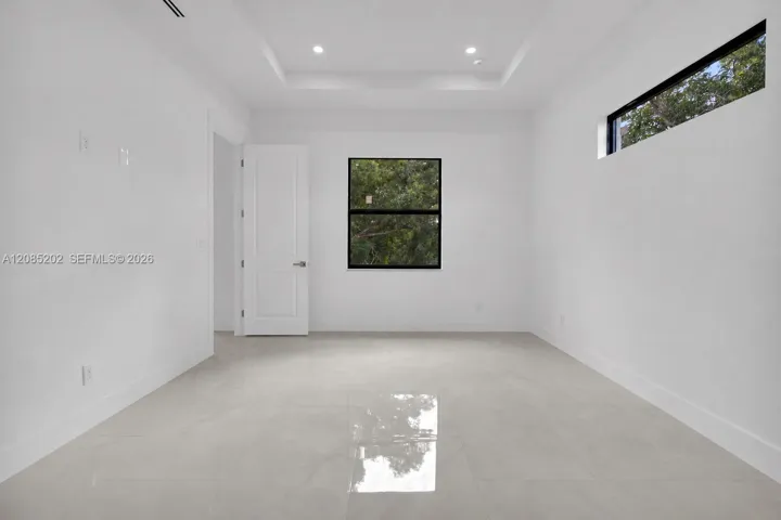 Interior room featuring large-format tile flooring, a tray ceiling with recessed lighting, black-framed windows, and a classic panel door